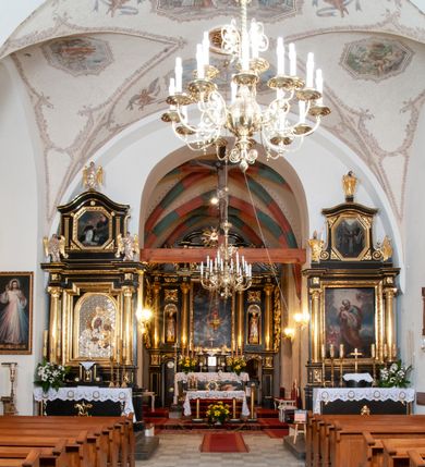 Zdjęcie nr 11: Na miejscu kościoła romańskiego, orientowany, dwunawowy, halowy; nawa południowa na rzucie prostokąta, na osi prezbiterium, dwuprzęsłowa, sklepiona kolebkowo z lunetami, na gurtach; nawa północna węższa od południowej, dwuprzęsłowa, sklepiona krzyżowo-żebrowo z kolistymi płaskorzeźbionymi zwornikami, jeden z literami ihs, drugi z literą s pod koroną. Prezbiterium prostokątne, dwuprzęsłowe, sklepione krzyżowo-żebrowo, z kolistymi zwornikami i profilowanymi wspornikami; przy nim od północy dawna zakrystia na rzucie prostokąta, sklepiona kolebkowo, otwarta do nawy wtórną arkadą, od wschodu nowa zakrystia na rzucie ośmioboku. Od zachodu przylega do nawy kwadratowa, czterokondygnacyjna wieża, z wieżyczką schodową w narożu północno-wschodnim, kruchtą w przyziemiu i chórem muzycznym na piętrze. Przy niej od północy drewniana piętrowa przybudówka mieszcząca w przyziemiu komorę bracką, na piętrze miech i kanał organowy. Przy nawie południowej od południa kwadratowa kruchta. Arkada tęczy zamknięta łukiem półkolistym, arkady do nawy północnej łukiem lekko zaostrzonym. Mury opięte przyporami, elewacje na cokole, z wzorami z zendrówki. Okna pierwotnie ostrołukowe, obustronnie rozglifione (niektóre zbarokizowane). Portale: zachodni, do kruchty pod wieżą, oraz do kruchty południowej, kamienne, prostokątne. Dachy dwuspadowe, pokryte blachą miedzianą. Zakrystia od wschodu przy prezbiterium wzniesiona na miejscu drewnianej kaplicy Ogrojcowej z XVIII wieku.