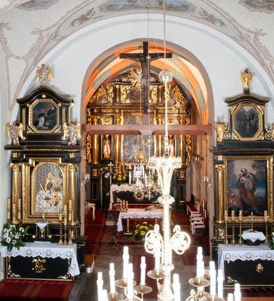 Zdjęcie nr 15: Na miejscu kościoła romańskiego, orientowany, dwunawowy, halowy; nawa południowa na rzucie prostokąta, na osi prezbiterium, dwuprzęsłowa, sklepiona kolebkowo z lunetami, na gurtach; nawa północna węższa od południowej, dwuprzęsłowa, sklepiona krzyżowo-żebrowo z kolistymi płaskorzeźbionymi zwornikami, jeden z literami ihs, drugi z literą s pod koroną. Prezbiterium prostokątne, dwuprzęsłowe, sklepione krzyżowo-żebrowo, z kolistymi zwornikami i profilowanymi wspornikami; przy nim od północy dawna zakrystia na rzucie prostokąta, sklepiona kolebkowo, otwarta do nawy wtórną arkadą, od wschodu nowa zakrystia na rzucie ośmioboku. Od zachodu przylega do nawy kwadratowa, czterokondygnacyjna wieża, z wieżyczką schodową w narożu północno-wschodnim, kruchtą w przyziemiu i chórem muzycznym na piętrze. Przy niej od północy drewniana piętrowa przybudówka mieszcząca w przyziemiu komorę bracką, na piętrze miech i kanał organowy. Przy nawie południowej od południa kwadratowa kruchta. Arkada tęczy zamknięta łukiem półkolistym, arkady do nawy północnej łukiem lekko zaostrzonym. Mury opięte przyporami, elewacje na cokole, z wzorami z zendrówki. Okna pierwotnie ostrołukowe, obustronnie rozglifione (niektóre zbarokizowane). Portale: zachodni, do kruchty pod wieżą, oraz do kruchty południowej, kamienne, prostokątne. Dachy dwuspadowe, pokryte blachą miedzianą. Zakrystia od wschodu przy prezbiterium wzniesiona na miejscu drewnianej kaplicy Ogrojcowej z XVIII wieku.