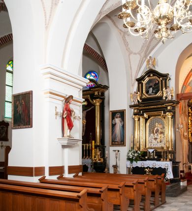 Zdjęcie nr 12: Na miejscu kościoła romańskiego, orientowany, dwunawowy, halowy; nawa południowa na rzucie prostokąta, na osi prezbiterium, dwuprzęsłowa, sklepiona kolebkowo z lunetami, na gurtach; nawa północna węższa od południowej, dwuprzęsłowa, sklepiona krzyżowo-żebrowo z kolistymi płaskorzeźbionymi zwornikami, jeden z literami ihs, drugi z literą s pod koroną. Prezbiterium prostokątne, dwuprzęsłowe, sklepione krzyżowo-żebrowo, z kolistymi zwornikami i profilowanymi wspornikami; przy nim od północy dawna zakrystia na rzucie prostokąta, sklepiona kolebkowo, otwarta do nawy wtórną arkadą, od wschodu nowa zakrystia na rzucie ośmioboku. Od zachodu przylega do nawy kwadratowa, czterokondygnacyjna wieża, z wieżyczką schodową w narożu północno-wschodnim, kruchtą w przyziemiu i chórem muzycznym na piętrze. Przy niej od północy drewniana piętrowa przybudówka mieszcząca w przyziemiu komorę bracką, na piętrze miech i kanał organowy. Przy nawie południowej od południa kwadratowa kruchta. Arkada tęczy zamknięta łukiem półkolistym, arkady do nawy północnej łukiem lekko zaostrzonym. Mury opięte przyporami, elewacje na cokole, z wzorami z zendrówki. Okna pierwotnie ostrołukowe, obustronnie rozglifione (niektóre zbarokizowane). Portale: zachodni, do kruchty pod wieżą, oraz do kruchty południowej, kamienne, prostokątne. Dachy dwuspadowe, pokryte blachą miedzianą. Zakrystia od wschodu przy prezbiterium wzniesiona na miejscu drewnianej kaplicy Ogrojcowej z XVIII wieku.