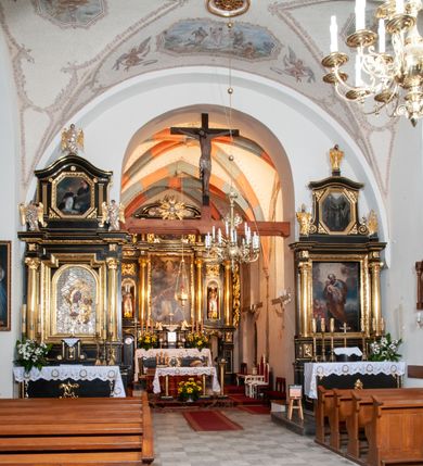 Zdjęcie nr 14: Na miejscu kościoła romańskiego, orientowany, dwunawowy, halowy; nawa południowa na rzucie prostokąta, na osi prezbiterium, dwuprzęsłowa, sklepiona kolebkowo z lunetami, na gurtach; nawa północna węższa od południowej, dwuprzęsłowa, sklepiona krzyżowo-żebrowo z kolistymi płaskorzeźbionymi zwornikami, jeden z literami ihs, drugi z literą s pod koroną. Prezbiterium prostokątne, dwuprzęsłowe, sklepione krzyżowo-żebrowo, z kolistymi zwornikami i profilowanymi wspornikami; przy nim od północy dawna zakrystia na rzucie prostokąta, sklepiona kolebkowo, otwarta do nawy wtórną arkadą, od wschodu nowa zakrystia na rzucie ośmioboku. Od zachodu przylega do nawy kwadratowa, czterokondygnacyjna wieża, z wieżyczką schodową w narożu północno-wschodnim, kruchtą w przyziemiu i chórem muzycznym na piętrze. Przy niej od północy drewniana piętrowa przybudówka mieszcząca w przyziemiu komorę bracką, na piętrze miech i kanał organowy. Przy nawie południowej od południa kwadratowa kruchta. Arkada tęczy zamknięta łukiem półkolistym, arkady do nawy północnej łukiem lekko zaostrzonym. Mury opięte przyporami, elewacje na cokole, z wzorami z zendrówki. Okna pierwotnie ostrołukowe, obustronnie rozglifione (niektóre zbarokizowane). Portale: zachodni, do kruchty pod wieżą, oraz do kruchty południowej, kamienne, prostokątne. Dachy dwuspadowe, pokryte blachą miedzianą. Zakrystia od wschodu przy prezbiterium wzniesiona na miejscu drewnianej kaplicy Ogrojcowej z XVIII wieku.