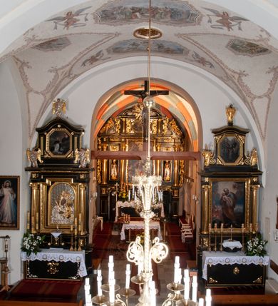 Zdjęcie nr 18: Na miejscu kościoła romańskiego, orientowany, dwunawowy, halowy; nawa południowa na rzucie prostokąta, na osi prezbiterium, dwuprzęsłowa, sklepiona kolebkowo z lunetami, na gurtach; nawa północna węższa od południowej, dwuprzęsłowa, sklepiona krzyżowo-żebrowo z kolistymi płaskorzeźbionymi zwornikami, jeden z literami ihs, drugi z literą s pod koroną. Prezbiterium prostokątne, dwuprzęsłowe, sklepione krzyżowo-żebrowo, z kolistymi zwornikami i profilowanymi wspornikami; przy nim od północy dawna zakrystia na rzucie prostokąta, sklepiona kolebkowo, otwarta do nawy wtórną arkadą, od wschodu nowa zakrystia na rzucie ośmioboku. Od zachodu przylega do nawy kwadratowa, czterokondygnacyjna wieża, z wieżyczką schodową w narożu północno-wschodnim, kruchtą w przyziemiu i chórem muzycznym na piętrze. Przy niej od północy drewniana piętrowa przybudówka mieszcząca w przyziemiu komorę bracką, na piętrze miech i kanał organowy. Przy nawie południowej od południa kwadratowa kruchta. Arkada tęczy zamknięta łukiem półkolistym, arkady do nawy północnej łukiem lekko zaostrzonym. Mury opięte przyporami, elewacje na cokole, z wzorami z zendrówki. Okna pierwotnie ostrołukowe, obustronnie rozglifione (niektóre zbarokizowane). Portale: zachodni, do kruchty pod wieżą, oraz do kruchty południowej, kamienne, prostokątne. Dachy dwuspadowe, pokryte blachą miedzianą. Zakrystia od wschodu przy prezbiterium wzniesiona na miejscu drewnianej kaplicy Ogrojcowej z XVIII wieku.