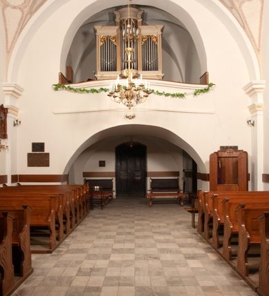 Zdjęcie nr 36: Na miejscu kościoła romańskiego, orientowany, dwunawowy, halowy; nawa południowa na rzucie prostokąta, na osi prezbiterium, dwuprzęsłowa, sklepiona kolebkowo z lunetami, na gurtach; nawa północna węższa od południowej, dwuprzęsłowa, sklepiona krzyżowo-żebrowo z kolistymi płaskorzeźbionymi zwornikami, jeden z literami ihs, drugi z literą s pod koroną. Prezbiterium prostokątne, dwuprzęsłowe, sklepione krzyżowo-żebrowo, z kolistymi zwornikami i profilowanymi wspornikami; przy nim od północy dawna zakrystia na rzucie prostokąta, sklepiona kolebkowo, otwarta do nawy wtórną arkadą, od wschodu nowa zakrystia na rzucie ośmioboku. Od zachodu przylega do nawy kwadratowa, czterokondygnacyjna wieża, z wieżyczką schodową w narożu północno-wschodnim, kruchtą w przyziemiu i chórem muzycznym na piętrze. Przy niej od północy drewniana piętrowa przybudówka mieszcząca w przyziemiu komorę bracką, na piętrze miech i kanał organowy. Przy nawie południowej od południa kwadratowa kruchta. Arkada tęczy zamknięta łukiem półkolistym, arkady do nawy północnej łukiem lekko zaostrzonym. Mury opięte przyporami, elewacje na cokole, z wzorami z zendrówki. Okna pierwotnie ostrołukowe, obustronnie rozglifione (niektóre zbarokizowane). Portale: zachodni, do kruchty pod wieżą, oraz do kruchty południowej, kamienne, prostokątne. Dachy dwuspadowe, pokryte blachą miedzianą. Zakrystia od wschodu przy prezbiterium wzniesiona na miejscu drewnianej kaplicy Ogrojcowej z XVIII wieku.