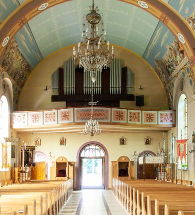 Zdjęcie nr 11: Kościół murowany, na kamiennym podmurowaniu, jednonawowy, na planie krzyża. Nawa na rzucie wydłużonego prostokąta, z węższym, jednoprzęsłowym prezbiterium zamkniętym trójbocznie, flankowanym dwoma kwadratowymi aneksami – zakrystią i kaplicą. Od południowego-zachodu dostawiona wieża na planie kwadratu z uskokowym zwężeniem ostatniej kondygnacji, z kruchtą w przyziemiu, ujęta dwiema wieżyczkami na planie ściętego koła, w południowej kręcone schody, w północnej schowek oraz dwoma otwartymi na zewnątrz arkadą aneksami na planie kwadratu z wejściami bocznymi do świątyni. Wnętrze nakryte sklepieniem kolebkowym z dwoma gurtami opadającymi na cztery półfilary. Otwór tęczowy w formie leżącego prostokąta zamkniętego łukiem półkolistym. W południowo-zachodniej części nawy zawieszony parapet chóru muzycznego o wybrzuszonej części środkowej balustrady. Posadzka betonowa, pokryta płytami kamiennymi. Fasada wieżowa, bez podziału na kondygnacje, w narożach ujęta kamiennymi szkarpami. Na osi portal wejściowy w formie kwadratu zamkniętego łukiem półkolistym, z dwuskrzydłowymi drzwiami, nakryty daszkiem okapowym. Nad nim okno witrażowe w formie koła. Wieża przepruta z trzech stron oknami w formie wydłużonego prostokąta zamkniętego półkoliście oraz w najwyższej części z czterech stron potrójnymi, arkadkowymi oknami. Wieżyczki przeprute niewielkimi, okrągłymi okienkami. Elewacje północna i południowa, ujęte we frontowych narożach kamiennymi szkarpami, przeprute trzema oknami witrażowymi w formie wydłużonego prostokąta zamkniętego półkoliście. Kaplica i zakrystia z jednym oknem o kształcie kwadratu zamkniętego łukiem półkolistym. Elewacja północno-wschodnia z dwoma oknami. Wieża nakryta dachem wieżowym kopulastym z latarnią zakończoną krzyżem, wieżyczki daszkami stożkowymi, a aneksy pulpitowymi. Dach nad nawą dwuspadowy z sześcioboczną wieżyczką na sygnaturkę nakrytą daszkiem wieżowym, prezbiterium niższe, przykryte dachem wielospadowym, kaplica i zakrystia dwuspadowym. 