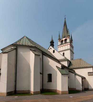 Zdjęcie nr 9: Kościół orientowany, murowany, trójnawowy, z prezbiterium zamkniętym trójbocznie, zakrystią od północy i kruchtą od południa. Do naw przylegają kaplice: większa od północy i mniejsza od południa. Dwie kolejne kaplice przylegają do boków wieży. Ściany wnętrza gładkie, pokryte polichromią imitującą podziały i obramienia, dekorację ornamentalną i sceny iluzjonistyczne na stropach, utrzymane w chłodnej biało-niebiesko-różowej tonacji z dodatkiem żółtego. Na stropie prezbiterium scena Zwiastowania, na stropie nawy Zesłania Ducha Świętego. Od zachodu chór muzyczny wsparty na dwóch filarach z balustradą pokrytą polichromią. Prezbiterium i nawa główna nakryte stropami, nad prezbiterium o przekroju spłaszczonej kolebki, nad nawą płaski, z szerokimi fasetami, zakrystia sklepiona kolebkowo, kruchta i kaplice wschodnie krzyżowo. Nawę, prezbiterium i część kaplic doświetlają okna w kształcie stojącego prostokąta zamkniętego łukiem pełnym, pozostałe zamknięte łukiem odcinkowym lub kwadratowe. Główne wejście i dwa boczne od zachodu, kolejne do przedsionka od północy i do kruchty od południa. Fasada z wieżą na osi, poprzedzona portykiem wspartym na filarach, z trójkątnym szczytem zwieńczonym krzyżem łacińskim. Fasada jednokondygnacyjna, przechodząca w masyw wieży. Kondygnację przepruwają trzy okna i jest zamknięta gzymsem wyniesionym na środku w łuk. Wieńczący ją trójkątny szczyt wtapia się w kondygnację wieży o gładkich elewacjach przeprutych jedynie niewielkimi oknami i tarczami zegarów. Ostatnia kondygnacja jest ujęta gzymsami i dekorowana fryzem arkadowym, którego arkady wykonano z nietynkowanej cegły. Zwieńczenie rozbudowane składa się z iglicy i ustawionych wokół niej, w narożach małych, dwukondygnacyjnych wieżyczek zamkniętych dachami stożkowymi. Wieżyczki połączono podwójnymi arkadami, których łuki wykonano z nietynkowanej cegły, tak samo jak górne kondygnacje wieżyczek. Elewacje kościoła gładkie, na niskim, kamiennym cokole, od wschodu opięte szkarpami. Prezbiterium i nawę przekrywają osobne dachy dwuspadowe, na kalenicy nawy wieżyczka na sygnaturkę, cztery kaplice i portyk nakrywają dachy trójpołaciowe, zakrystię i nawy boczne pulpitowe. 
Jedyne zachowane elementy wyposażenia sprzed pożaru w 1815 roku to fragment osiemnastowiecznej polichromii przedstawiającej dwóch aniołów z narzędziami męki i przedmioty nawiązujące do tego wydarzenia oraz gotycki portal do zakrystii wraz z żelaznymi, kutymi drzwiami. 
