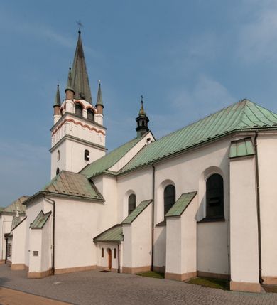 Zdjęcie nr 6: Kościół orientowany, murowany, trójnawowy, z prezbiterium zamkniętym trójbocznie, zakrystią od północy i kruchtą od południa. Do naw przylegają kaplice: większa od północy i mniejsza od południa. Dwie kolejne kaplice przylegają do boków wieży. Ściany wnętrza gładkie, pokryte polichromią imitującą podziały i obramienia, dekorację ornamentalną i sceny iluzjonistyczne na stropach, utrzymane w chłodnej biało-niebiesko-różowej tonacji z dodatkiem żółtego. Na stropie prezbiterium scena Zwiastowania, na stropie nawy Zesłania Ducha Świętego. Od zachodu chór muzyczny wsparty na dwóch filarach z balustradą pokrytą polichromią. Prezbiterium i nawa główna nakryte stropami, nad prezbiterium o przekroju spłaszczonej kolebki, nad nawą płaski, z szerokimi fasetami, zakrystia sklepiona kolebkowo, kruchta i kaplice wschodnie krzyżowo. Nawę, prezbiterium i część kaplic doświetlają okna w kształcie stojącego prostokąta zamkniętego łukiem pełnym, pozostałe zamknięte łukiem odcinkowym lub kwadratowe. Główne wejście i dwa boczne od zachodu, kolejne do przedsionka od północy i do kruchty od południa. Fasada z wieżą na osi, poprzedzona portykiem wspartym na filarach, z trójkątnym szczytem zwieńczonym krzyżem łacińskim. Fasada jednokondygnacyjna, przechodząca w masyw wieży. Kondygnację przepruwają trzy okna i jest zamknięta gzymsem wyniesionym na środku w łuk. Wieńczący ją trójkątny szczyt wtapia się w kondygnację wieży o gładkich elewacjach przeprutych jedynie niewielkimi oknami i tarczami zegarów. Ostatnia kondygnacja jest ujęta gzymsami i dekorowana fryzem arkadowym, którego arkady wykonano z nietynkowanej cegły. Zwieńczenie rozbudowane składa się z iglicy i ustawionych wokół niej, w narożach małych, dwukondygnacyjnych wieżyczek zamkniętych dachami stożkowymi. Wieżyczki połączono podwójnymi arkadami, których łuki wykonano z nietynkowanej cegły, tak samo jak górne kondygnacje wieżyczek. Elewacje kościoła gładkie, na niskim, kamiennym cokole, od wschodu opięte szkarpami. Prezbiterium i nawę przekrywają osobne dachy dwuspadowe, na kalenicy nawy wieżyczka na sygnaturkę, cztery kaplice i portyk nakrywają dachy trójpołaciowe, zakrystię i nawy boczne pulpitowe. 
Jedyne zachowane elementy wyposażenia sprzed pożaru w 1815 roku to fragment osiemnastowiecznej polichromii przedstawiającej dwóch aniołów z narzędziami męki i przedmioty nawiązujące do tego wydarzenia oraz gotycki portal do zakrystii wraz z żelaznymi, kutymi drzwiami. 
