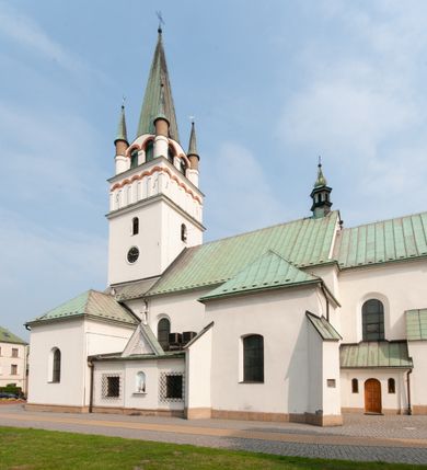 Zdjęcie nr 4: Kościół orientowany, murowany, trójnawowy, z prezbiterium zamkniętym trójbocznie, zakrystią od północy i kruchtą od południa. Do naw przylegają kaplice: większa od północy i mniejsza od południa. Dwie kolejne kaplice przylegają do boków wieży. Ściany wnętrza gładkie, pokryte polichromią imitującą podziały i obramienia, dekorację ornamentalną i sceny iluzjonistyczne na stropach, utrzymane w chłodnej biało-niebiesko-różowej tonacji z dodatkiem żółtego. Na stropie prezbiterium scena Zwiastowania, na stropie nawy Zesłania Ducha Świętego. Od zachodu chór muzyczny wsparty na dwóch filarach z balustradą pokrytą polichromią. Prezbiterium i nawa główna nakryte stropami, nad prezbiterium o przekroju spłaszczonej kolebki, nad nawą płaski, z szerokimi fasetami, zakrystia sklepiona kolebkowo, kruchta i kaplice wschodnie krzyżowo. Nawę, prezbiterium i część kaplic doświetlają okna w kształcie stojącego prostokąta zamkniętego łukiem pełnym, pozostałe zamknięte łukiem odcinkowym lub kwadratowe. Główne wejście i dwa boczne od zachodu, kolejne do przedsionka od północy i do kruchty od południa. Fasada z wieżą na osi, poprzedzona portykiem wspartym na filarach, z trójkątnym szczytem zwieńczonym krzyżem łacińskim. Fasada jednokondygnacyjna, przechodząca w masyw wieży. Kondygnację przepruwają trzy okna i jest zamknięta gzymsem wyniesionym na środku w łuk. Wieńczący ją trójkątny szczyt wtapia się w kondygnację wieży o gładkich elewacjach przeprutych jedynie niewielkimi oknami i tarczami zegarów. Ostatnia kondygnacja jest ujęta gzymsami i dekorowana fryzem arkadowym, którego arkady wykonano z nietynkowanej cegły. Zwieńczenie rozbudowane składa się z iglicy i ustawionych wokół niej, w narożach małych, dwukondygnacyjnych wieżyczek zamkniętych dachami stożkowymi. Wieżyczki połączono podwójnymi arkadami, których łuki wykonano z nietynkowanej cegły, tak samo jak górne kondygnacje wieżyczek. Elewacje kościoła gładkie, na niskim, kamiennym cokole, od wschodu opięte szkarpami. Prezbiterium i nawę przekrywają osobne dachy dwuspadowe, na kalenicy nawy wieżyczka na sygnaturkę, cztery kaplice i portyk nakrywają dachy trójpołaciowe, zakrystię i nawy boczne pulpitowe. 
Jedyne zachowane elementy wyposażenia sprzed pożaru w 1815 roku to fragment osiemnastowiecznej polichromii przedstawiającej dwóch aniołów z narzędziami męki i przedmioty nawiązujące do tego wydarzenia oraz gotycki portal do zakrystii wraz z żelaznymi, kutymi drzwiami. 
