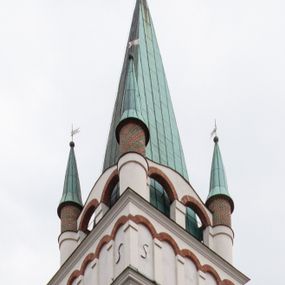 Zdjęcie nr 1: Kościół orientowany, murowany, trójnawowy, z prezbiterium zamkniętym trójbocznie, zakrystią od północy i kruchtą od południa. Do naw przylegają kaplice: większa od północy i mniejsza od południa. Dwie kolejne kaplice przylegają do boków wieży. Ściany wnętrza gładkie, pokryte polichromią imitującą podziały i obramienia, dekorację ornamentalną i sceny iluzjonistyczne na stropach, utrzymane w chłodnej biało-niebiesko-różowej tonacji z dodatkiem żółtego. Na stropie prezbiterium scena Zwiastowania, na stropie nawy Zesłania Ducha Świętego. Od zachodu chór muzyczny wsparty na dwóch filarach z balustradą pokrytą polichromią. Prezbiterium i nawa główna nakryte stropami, nad prezbiterium o przekroju spłaszczonej kolebki, nad nawą płaski, z szerokimi fasetami, zakrystia sklepiona kolebkowo, kruchta i kaplice wschodnie krzyżowo. Nawę, prezbiterium i część kaplic doświetlają okna w kształcie stojącego prostokąta zamkniętego łukiem pełnym, pozostałe zamknięte łukiem odcinkowym lub kwadratowe. Główne wejście i dwa boczne od zachodu, kolejne do przedsionka od północy i do kruchty od południa. Fasada z wieżą na osi, poprzedzona portykiem wspartym na filarach, z trójkątnym szczytem zwieńczonym krzyżem łacińskim. Fasada jednokondygnacyjna, przechodząca w masyw wieży. Kondygnację przepruwają trzy okna i jest zamknięta gzymsem wyniesionym na środku w łuk. Wieńczący ją trójkątny szczyt wtapia się w kondygnację wieży o gładkich elewacjach przeprutych jedynie niewielkimi oknami i tarczami zegarów. Ostatnia kondygnacja jest ujęta gzymsami i dekorowana fryzem arkadowym, którego arkady wykonano z nietynkowanej cegły. Zwieńczenie rozbudowane składa się z iglicy i ustawionych wokół niej, w narożach małych, dwukondygnacyjnych wieżyczek zamkniętych dachami stożkowymi. Wieżyczki połączono podwójnymi arkadami, których łuki wykonano z nietynkowanej cegły, tak samo jak górne kondygnacje wieżyczek. Elewacje kościoła gładkie, na niskim, kamiennym cokole, od wschodu opięte szkarpami. Prezbiterium i nawę przekrywają osobne dachy dwuspadowe, na kalenicy nawy wieżyczka na sygnaturkę, cztery kaplice i portyk nakrywają dachy trójpołaciowe, zakrystię i nawy boczne pulpitowe. 
Jedyne zachowane elementy wyposażenia sprzed pożaru w 1815 roku to fragment osiemnastowiecznej polichromii przedstawiającej dwóch aniołów z narzędziami męki i przedmioty nawiązujące do tego wydarzenia oraz gotycki portal do zakrystii wraz z żelaznymi, kutymi drzwiami. 
