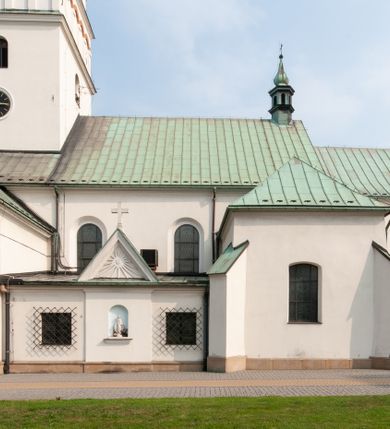 Zdjęcie nr 8: Kościół orientowany, murowany, trójnawowy, z prezbiterium zamkniętym trójbocznie, zakrystią od północy i kruchtą od południa. Do naw przylegają kaplice: większa od północy i mniejsza od południa. Dwie kolejne kaplice przylegają do boków wieży. Ściany wnętrza gładkie, pokryte polichromią imitującą podziały i obramienia, dekorację ornamentalną i sceny iluzjonistyczne na stropach, utrzymane w chłodnej biało-niebiesko-różowej tonacji z dodatkiem żółtego. Na stropie prezbiterium scena Zwiastowania, na stropie nawy Zesłania Ducha Świętego. Od zachodu chór muzyczny wsparty na dwóch filarach z balustradą pokrytą polichromią. Prezbiterium i nawa główna nakryte stropami, nad prezbiterium o przekroju spłaszczonej kolebki, nad nawą płaski, z szerokimi fasetami, zakrystia sklepiona kolebkowo, kruchta i kaplice wschodnie krzyżowo. Nawę, prezbiterium i część kaplic doświetlają okna w kształcie stojącego prostokąta zamkniętego łukiem pełnym, pozostałe zamknięte łukiem odcinkowym lub kwadratowe. Główne wejście i dwa boczne od zachodu, kolejne do przedsionka od północy i do kruchty od południa. Fasada z wieżą na osi, poprzedzona portykiem wspartym na filarach, z trójkątnym szczytem zwieńczonym krzyżem łacińskim. Fasada jednokondygnacyjna, przechodząca w masyw wieży. Kondygnację przepruwają trzy okna i jest zamknięta gzymsem wyniesionym na środku w łuk. Wieńczący ją trójkątny szczyt wtapia się w kondygnację wieży o gładkich elewacjach przeprutych jedynie niewielkimi oknami i tarczami zegarów. Ostatnia kondygnacja jest ujęta gzymsami i dekorowana fryzem arkadowym, którego arkady wykonano z nietynkowanej cegły. Zwieńczenie rozbudowane składa się z iglicy i ustawionych wokół niej, w narożach małych, dwukondygnacyjnych wieżyczek zamkniętych dachami stożkowymi. Wieżyczki połączono podwójnymi arkadami, których łuki wykonano z nietynkowanej cegły, tak samo jak górne kondygnacje wieżyczek. Elewacje kościoła gładkie, na niskim, kamiennym cokole, od wschodu opięte szkarpami. Prezbiterium i nawę przekrywają osobne dachy dwuspadowe, na kalenicy nawy wieżyczka na sygnaturkę, cztery kaplice i portyk nakrywają dachy trójpołaciowe, zakrystię i nawy boczne pulpitowe. 
Jedyne zachowane elementy wyposażenia sprzed pożaru w 1815 roku to fragment osiemnastowiecznej polichromii przedstawiającej dwóch aniołów z narzędziami męki i przedmioty nawiązujące do tego wydarzenia oraz gotycki portal do zakrystii wraz z żelaznymi, kutymi drzwiami. 
