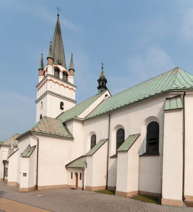 Zdjęcie nr 5: Kościół orientowany, murowany, trójnawowy, z prezbiterium zamkniętym trójbocznie, zakrystią od północy i kruchtą od południa. Do naw przylegają kaplice: większa od północy i mniejsza od południa. Dwie kolejne kaplice przylegają do boków wieży. Ściany wnętrza gładkie, pokryte polichromią imitującą podziały i obramienia, dekorację ornamentalną i sceny iluzjonistyczne na stropach, utrzymane w chłodnej biało-niebiesko-różowej tonacji z dodatkiem żółtego. Na stropie prezbiterium scena Zwiastowania, na stropie nawy Zesłania Ducha Świętego. Od zachodu chór muzyczny wsparty na dwóch filarach z balustradą pokrytą polichromią. Prezbiterium i nawa główna nakryte stropami, nad prezbiterium o przekroju spłaszczonej kolebki, nad nawą płaski, z szerokimi fasetami, zakrystia sklepiona kolebkowo, kruchta i kaplice wschodnie krzyżowo. Nawę, prezbiterium i część kaplic doświetlają okna w kształcie stojącego prostokąta zamkniętego łukiem pełnym, pozostałe zamknięte łukiem odcinkowym lub kwadratowe. Główne wejście i dwa boczne od zachodu, kolejne do przedsionka od północy i do kruchty od południa. Fasada z wieżą na osi, poprzedzona portykiem wspartym na filarach, z trójkątnym szczytem zwieńczonym krzyżem łacińskim. Fasada jednokondygnacyjna, przechodząca w masyw wieży. Kondygnację przepruwają trzy okna i jest zamknięta gzymsem wyniesionym na środku w łuk. Wieńczący ją trójkątny szczyt wtapia się w kondygnację wieży o gładkich elewacjach przeprutych jedynie niewielkimi oknami i tarczami zegarów. Ostatnia kondygnacja jest ujęta gzymsami i dekorowana fryzem arkadowym, którego arkady wykonano z nietynkowanej cegły. Zwieńczenie rozbudowane składa się z iglicy i ustawionych wokół niej, w narożach małych, dwukondygnacyjnych wieżyczek zamkniętych dachami stożkowymi. Wieżyczki połączono podwójnymi arkadami, których łuki wykonano z nietynkowanej cegły, tak samo jak górne kondygnacje wieżyczek. Elewacje kościoła gładkie, na niskim, kamiennym cokole, od wschodu opięte szkarpami. Prezbiterium i nawę przekrywają osobne dachy dwuspadowe, na kalenicy nawy wieżyczka na sygnaturkę, cztery kaplice i portyk nakrywają dachy trójpołaciowe, zakrystię i nawy boczne pulpitowe. 
Jedyne zachowane elementy wyposażenia sprzed pożaru w 1815 roku to fragment osiemnastowiecznej polichromii przedstawiającej dwóch aniołów z narzędziami męki i przedmioty nawiązujące do tego wydarzenia oraz gotycki portal do zakrystii wraz z żelaznymi, kutymi drzwiami. 
