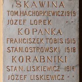 Zdjęcie nr 1: Tablica pamiątkowa z jasnego kamienia w kształcie bardzo wydłużonego, stojącego prostokąta, z kutym, złoconym napisem „SKAWINA / TOM(ASZ) HACHORKIEWICZ 1919 / JÓZEF LOREK / KOPANKA / FRANCISZEK TOBIS 1915 / STAI(ISŁAW) OSTROWSKI 1918 / KORABNIKI / STAN(ISŁAW) LISKIEWICZ 1914 / JÓZEF LISKIEWICZ / JAN KŁYŚ 1919 / RZOZÓW / JÓZEF PLANTA 1914 / JAN KUBAS 1915 / MICHAŁ MADEJ / ANTONI KLIMAS 1918 / MICHAŁ PUTAJ / SAMBOREK / PIOTR HABAS 1917 / SIDZINA / JAN STYRYLSKI 1914 / ANDRZEJ BYK / JÓZEF CHMURA / MICHAŁ BALON 1915 / FRANCISZEK BYK 1919”. W narożach ozdobne rozetki maskują miejsca mocowania.