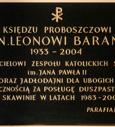 Zdjęcie nr 1: Tablica w kształcie leżącego prostokąta z kutym, złoconym napisem poniżej chrystogramu „KSIĘDZU PROBOSZCZOWI / KS(IĘDZU) KAN(ONIKOWI) LEONOWI BARANOWI / 1933-2004 / ZAŁOŻYCIELOWI ZESPOŁU KATOLICKICH SZKÓŁ / im(ienia) JANA PAWŁA II / ORAZ JADŁODAJNI DLA UBOGICH / Z WDZIĘCZNOŚCIĄ ZA POSŁUGĘ DUSZPASTERSKĄ / W SKAWINIE W LATACH 1983-2004 / PARAFIANIE”. W narożach dekoracyjne rozetki maskują miejsca mocowania. 