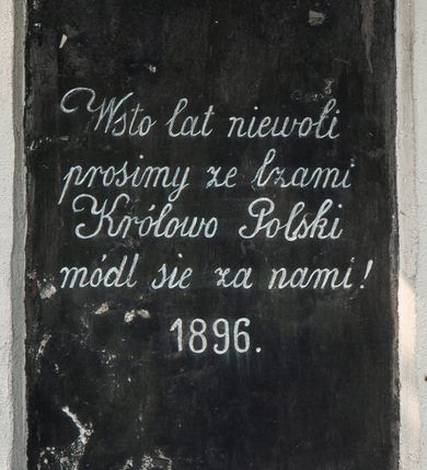 Zdjęcie nr 1: Tablica w kształcie stojącego prostokąta z bieloną inskrypcją „Wsto lat niewoli / prosimy ze łzami / Królowo Polski / módl się za nami ! / 1896”. 