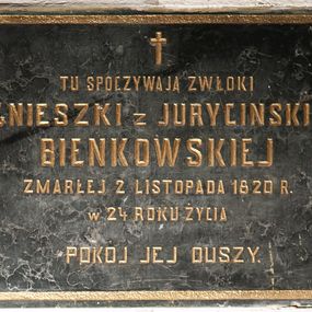 Zdjęcie nr 1: Tablica w kształcie leżącego prostokąta obwiedziona ramką z kwadratami w narożach. Na środku, poniżej krzyża łacińskiego złocona, majuskułowa inskrypcja „TU SPOCZYWAJĄ ZWŁOKI / AGNIESZKI z JURYCINSKICH / BIEŃKOWSKIEJ / ZMARŁEJ 2 LISTOPADA 1820 R(OKU) / W 24 ROKU ŻYCIA / POKÓJ JEJ DUSZY”. 