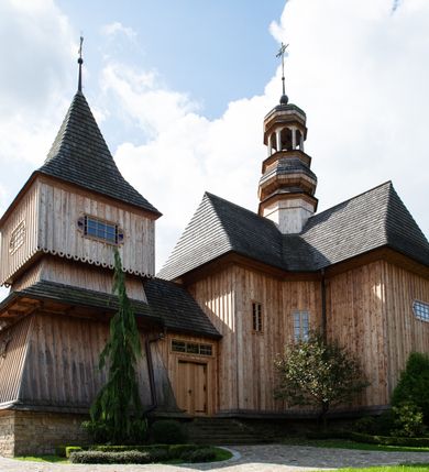 Zdjęcie nr 11: Kościół św. Joachima w Skawinkach usytuowany jest w centrum wsi, na zachód od głównej drogi prowadzącej z Palczy do Kalwarii Zebrzydowskiej. Teren przykościelny jest usytuowany na wysokim wzniesieniu, do którego prowadzą trzy wejścia, jedno przez schody, drugie przez obszerny wjazd od strony południowej.

Kościół skierowany na zachód, drewniany o konstrukcji zrębowej, na rzucie krzyża greckiego ze ściętymi kątami międzyramiennymi.  Przy prezbiterium zakrystia. Strop wsparty na czterech parach słupów, ustawionych w krzyżu kościoła, w licu ścian ramienia wschodniego i zachodniego. Belka tęczy prosta, profilowana na kroksztynach, na niej Grupa Ukrzyżowania. Świątynia połączona za pomocą kruchty z wieżą o konstrukcji słupowej, na planie kwadratu z nadwieszoną izbicą, nakryta dachem namiotowym, ściany dzwonnicy opasane mniej więcej w połowie wysokości pulpitowym daszkiem, zlewającym się po bokach z siodłowym dachem kruchty. Do kościoła prowadzi główne wejście w przedsionku od strony południowej. Wnętrze świątyni oświetlają prostokątne okna. Dach nakryty gontem, na skrzyżowaniu ramiona krzyża greckiego wystawiona wieżyczka na sygnaturkę z latarnią. Ściany na zewnątrz pokryte szalunkiem pionowym.
