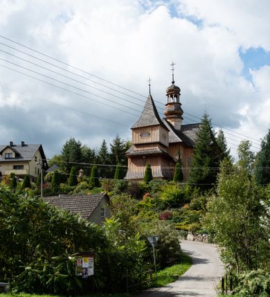 Zdjęcie nr 18: Kościół św. Joachima w Skawinkach usytuowany jest w centrum wsi, na zachód od głównej drogi prowadzącej z Palczy do Kalwarii Zebrzydowskiej. Teren przykościelny jest usytuowany na wysokim wzniesieniu, do którego prowadzą trzy wejścia, jedno przez schody, drugie przez obszerny wjazd od strony południowej.

Kościół skierowany na zachód, drewniany o konstrukcji zrębowej, na rzucie krzyża greckiego ze ściętymi kątami międzyramiennymi.  Przy prezbiterium zakrystia. Strop wsparty na czterech parach słupów, ustawionych w krzyżu kościoła, w licu ścian ramienia wschodniego i zachodniego. Belka tęczy prosta, profilowana na kroksztynach, na niej Grupa Ukrzyżowania. Świątynia połączona za pomocą kruchty z wieżą o konstrukcji słupowej, na planie kwadratu z nadwieszoną izbicą, nakryta dachem namiotowym, ściany dzwonnicy opasane mniej więcej w połowie wysokości pulpitowym daszkiem, zlewającym się po bokach z siodłowym dachem kruchty. Do kościoła prowadzi główne wejście w przedsionku od strony południowej. Wnętrze świątyni oświetlają prostokątne okna. Dach nakryty gontem, na skrzyżowaniu ramiona krzyża greckiego wystawiona wieżyczka na sygnaturkę z latarnią. Ściany na zewnątrz pokryte szalunkiem pionowym.
