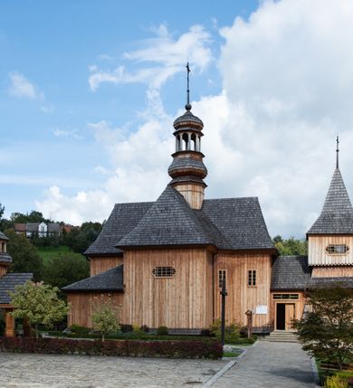 Zdjęcie nr 15: Kościół św. Joachima w Skawinkach usytuowany jest w centrum wsi, na zachód od głównej drogi prowadzącej z Palczy do Kalwarii Zebrzydowskiej. Teren przykościelny jest usytuowany na wysokim wzniesieniu, do którego prowadzą trzy wejścia, jedno przez schody, drugie przez obszerny wjazd od strony południowej.

Kościół skierowany na zachód, drewniany o konstrukcji zrębowej, na rzucie krzyża greckiego ze ściętymi kątami międzyramiennymi.  Przy prezbiterium zakrystia. Strop wsparty na czterech parach słupów, ustawionych w krzyżu kościoła, w licu ścian ramienia wschodniego i zachodniego. Belka tęczy prosta, profilowana na kroksztynach, na niej Grupa Ukrzyżowania. Świątynia połączona za pomocą kruchty z wieżą o konstrukcji słupowej, na planie kwadratu z nadwieszoną izbicą, nakryta dachem namiotowym, ściany dzwonnicy opasane mniej więcej w połowie wysokości pulpitowym daszkiem, zlewającym się po bokach z siodłowym dachem kruchty. Do kościoła prowadzi główne wejście w przedsionku od strony południowej. Wnętrze świątyni oświetlają prostokątne okna. Dach nakryty gontem, na skrzyżowaniu ramiona krzyża greckiego wystawiona wieżyczka na sygnaturkę z latarnią. Ściany na zewnątrz pokryte szalunkiem pionowym.
