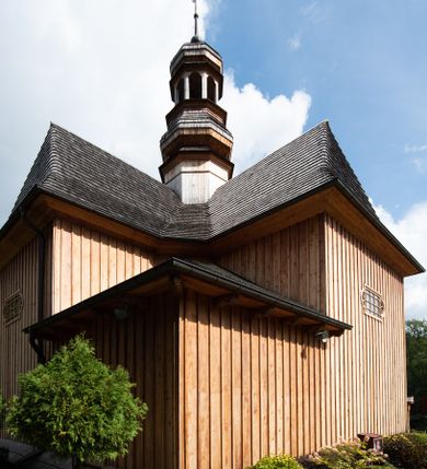 Zdjęcie nr 21: Kościół św. Joachima w Skawinkach usytuowany jest w centrum wsi, na zachód od głównej drogi prowadzącej z Palczy do Kalwarii Zebrzydowskiej. Teren przykościelny jest usytuowany na wysokim wzniesieniu, do którego prowadzą trzy wejścia, jedno przez schody, drugie przez obszerny wjazd od strony południowej.

Kościół skierowany na zachód, drewniany o konstrukcji zrębowej, na rzucie krzyża greckiego ze ściętymi kątami międzyramiennymi.  Przy prezbiterium zakrystia. Strop wsparty na czterech parach słupów, ustawionych w krzyżu kościoła, w licu ścian ramienia wschodniego i zachodniego. Belka tęczy prosta, profilowana na kroksztynach, na niej Grupa Ukrzyżowania. Świątynia połączona za pomocą kruchty z wieżą o konstrukcji słupowej, na planie kwadratu z nadwieszoną izbicą, nakryta dachem namiotowym, ściany dzwonnicy opasane mniej więcej w połowie wysokości pulpitowym daszkiem, zlewającym się po bokach z siodłowym dachem kruchty. Do kościoła prowadzi główne wejście w przedsionku od strony południowej. Wnętrze świątyni oświetlają prostokątne okna. Dach nakryty gontem, na skrzyżowaniu ramiona krzyża greckiego wystawiona wieżyczka na sygnaturkę z latarnią. Ściany na zewnątrz pokryte szalunkiem pionowym.
