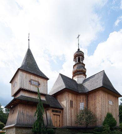 Zdjęcie nr 26: Kościół św. Joachima w Skawinkach usytuowany jest w centrum wsi, na zachód od głównej drogi prowadzącej z Palczy do Kalwarii Zebrzydowskiej. Teren przykościelny jest usytuowany na wysokim wzniesieniu, do którego prowadzą trzy wejścia, jedno przez schody, drugie przez obszerny wjazd od strony południowej.

Kościół skierowany na zachód, drewniany o konstrukcji zrębowej, na rzucie krzyża greckiego ze ściętymi kątami międzyramiennymi.  Przy prezbiterium zakrystia. Strop wsparty na czterech parach słupów, ustawionych w krzyżu kościoła, w licu ścian ramienia wschodniego i zachodniego. Belka tęczy prosta, profilowana na kroksztynach, na niej Grupa Ukrzyżowania. Świątynia połączona za pomocą kruchty z wieżą o konstrukcji słupowej, na planie kwadratu z nadwieszoną izbicą, nakryta dachem namiotowym, ściany dzwonnicy opasane mniej więcej w połowie wysokości pulpitowym daszkiem, zlewającym się po bokach z siodłowym dachem kruchty. Do kościoła prowadzi główne wejście w przedsionku od strony południowej. Wnętrze świątyni oświetlają prostokątne okna. Dach nakryty gontem, na skrzyżowaniu ramiona krzyża greckiego wystawiona wieżyczka na sygnaturkę z latarnią. Ściany na zewnątrz pokryte szalunkiem pionowym.
