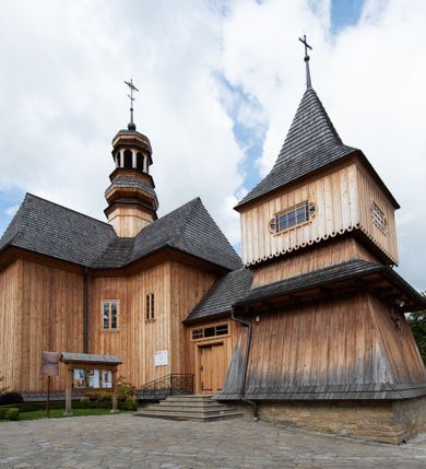 Zdjęcie nr 29: Kościół św. Joachima w Skawinkach usytuowany jest w centrum wsi, na zachód od głównej drogi prowadzącej z Palczy do Kalwarii Zebrzydowskiej. Teren przykościelny jest usytuowany na wysokim wzniesieniu, do którego prowadzą trzy wejścia, jedno przez schody, drugie przez obszerny wjazd od strony południowej.

Kościół skierowany na zachód, drewniany o konstrukcji zrębowej, na rzucie krzyża greckiego ze ściętymi kątami międzyramiennymi.  Przy prezbiterium zakrystia. Strop wsparty na czterech parach słupów, ustawionych w krzyżu kościoła, w licu ścian ramienia wschodniego i zachodniego. Belka tęczy prosta, profilowana na kroksztynach, na niej Grupa Ukrzyżowania. Świątynia połączona za pomocą kruchty z wieżą o konstrukcji słupowej, na planie kwadratu z nadwieszoną izbicą, nakryta dachem namiotowym, ściany dzwonnicy opasane mniej więcej w połowie wysokości pulpitowym daszkiem, zlewającym się po bokach z siodłowym dachem kruchty. Do kościoła prowadzi główne wejście w przedsionku od strony południowej. Wnętrze świątyni oświetlają prostokątne okna. Dach nakryty gontem, na skrzyżowaniu ramiona krzyża greckiego wystawiona wieżyczka na sygnaturkę z latarnią. Ściany na zewnątrz pokryte szalunkiem pionowym.
