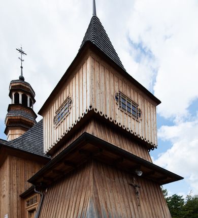 Zdjęcie nr 27: Kościół św. Joachima w Skawinkach usytuowany jest w centrum wsi, na zachód od głównej drogi prowadzącej z Palczy do Kalwarii Zebrzydowskiej. Teren przykościelny jest usytuowany na wysokim wzniesieniu, do którego prowadzą trzy wejścia, jedno przez schody, drugie przez obszerny wjazd od strony południowej.

Kościół skierowany na zachód, drewniany o konstrukcji zrębowej, na rzucie krzyża greckiego ze ściętymi kątami międzyramiennymi.  Przy prezbiterium zakrystia. Strop wsparty na czterech parach słupów, ustawionych w krzyżu kościoła, w licu ścian ramienia wschodniego i zachodniego. Belka tęczy prosta, profilowana na kroksztynach, na niej Grupa Ukrzyżowania. Świątynia połączona za pomocą kruchty z wieżą o konstrukcji słupowej, na planie kwadratu z nadwieszoną izbicą, nakryta dachem namiotowym, ściany dzwonnicy opasane mniej więcej w połowie wysokości pulpitowym daszkiem, zlewającym się po bokach z siodłowym dachem kruchty. Do kościoła prowadzi główne wejście w przedsionku od strony południowej. Wnętrze świątyni oświetlają prostokątne okna. Dach nakryty gontem, na skrzyżowaniu ramiona krzyża greckiego wystawiona wieżyczka na sygnaturkę z latarnią. Ściany na zewnątrz pokryte szalunkiem pionowym.
