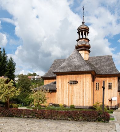 Zdjęcie nr 32: Kościół św. Joachima w Skawinkach usytuowany jest w centrum wsi, na zachód od głównej drogi prowadzącej z Palczy do Kalwarii Zebrzydowskiej. Teren przykościelny jest usytuowany na wysokim wzniesieniu, do którego prowadzą trzy wejścia, jedno przez schody, drugie przez obszerny wjazd od strony południowej.

Kościół skierowany na zachód, drewniany o konstrukcji zrębowej, na rzucie krzyża greckiego ze ściętymi kątami międzyramiennymi.  Przy prezbiterium zakrystia. Strop wsparty na czterech parach słupów, ustawionych w krzyżu kościoła, w licu ścian ramienia wschodniego i zachodniego. Belka tęczy prosta, profilowana na kroksztynach, na niej Grupa Ukrzyżowania. Świątynia połączona za pomocą kruchty z wieżą o konstrukcji słupowej, na planie kwadratu z nadwieszoną izbicą, nakryta dachem namiotowym, ściany dzwonnicy opasane mniej więcej w połowie wysokości pulpitowym daszkiem, zlewającym się po bokach z siodłowym dachem kruchty. Do kościoła prowadzi główne wejście w przedsionku od strony południowej. Wnętrze świątyni oświetlają prostokątne okna. Dach nakryty gontem, na skrzyżowaniu ramiona krzyża greckiego wystawiona wieżyczka na sygnaturkę z latarnią. Ściany na zewnątrz pokryte szalunkiem pionowym.
