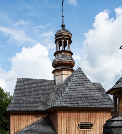 Zdjęcie nr 38: Kościół św. Joachima w Skawinkach usytuowany jest w centrum wsi, na zachód od głównej drogi prowadzącej z Palczy do Kalwarii Zebrzydowskiej. Teren przykościelny jest usytuowany na wysokim wzniesieniu, do którego prowadzą trzy wejścia, jedno przez schody, drugie przez obszerny wjazd od strony południowej.

Kościół skierowany na zachód, drewniany o konstrukcji zrębowej, na rzucie krzyża greckiego ze ściętymi kątami międzyramiennymi.  Przy prezbiterium zakrystia. Strop wsparty na czterech parach słupów, ustawionych w krzyżu kościoła, w licu ścian ramienia wschodniego i zachodniego. Belka tęczy prosta, profilowana na kroksztynach, na niej Grupa Ukrzyżowania. Świątynia połączona za pomocą kruchty z wieżą o konstrukcji słupowej, na planie kwadratu z nadwieszoną izbicą, nakryta dachem namiotowym, ściany dzwonnicy opasane mniej więcej w połowie wysokości pulpitowym daszkiem, zlewającym się po bokach z siodłowym dachem kruchty. Do kościoła prowadzi główne wejście w przedsionku od strony południowej. Wnętrze świątyni oświetlają prostokątne okna. Dach nakryty gontem, na skrzyżowaniu ramiona krzyża greckiego wystawiona wieżyczka na sygnaturkę z latarnią. Ściany na zewnątrz pokryte szalunkiem pionowym.
