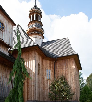 Zdjęcie nr 41: Kościół św. Joachima w Skawinkach usytuowany jest w centrum wsi, na zachód od głównej drogi prowadzącej z Palczy do Kalwarii Zebrzydowskiej. Teren przykościelny jest usytuowany na wysokim wzniesieniu, do którego prowadzą trzy wejścia, jedno przez schody, drugie przez obszerny wjazd od strony południowej.

Kościół skierowany na zachód, drewniany o konstrukcji zrębowej, na rzucie krzyża greckiego ze ściętymi kątami międzyramiennymi.  Przy prezbiterium zakrystia. Strop wsparty na czterech parach słupów, ustawionych w krzyżu kościoła, w licu ścian ramienia wschodniego i zachodniego. Belka tęczy prosta, profilowana na kroksztynach, na niej Grupa Ukrzyżowania. Świątynia połączona za pomocą kruchty z wieżą o konstrukcji słupowej, na planie kwadratu z nadwieszoną izbicą, nakryta dachem namiotowym, ściany dzwonnicy opasane mniej więcej w połowie wysokości pulpitowym daszkiem, zlewającym się po bokach z siodłowym dachem kruchty. Do kościoła prowadzi główne wejście w przedsionku od strony południowej. Wnętrze świątyni oświetlają prostokątne okna. Dach nakryty gontem, na skrzyżowaniu ramiona krzyża greckiego wystawiona wieżyczka na sygnaturkę z latarnią. Ściany na zewnątrz pokryte szalunkiem pionowym.
