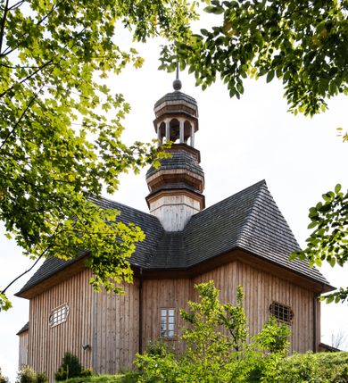 Zdjęcie nr 44: Kościół św. Joachima w Skawinkach usytuowany jest w centrum wsi, na zachód od głównej drogi prowadzącej z Palczy do Kalwarii Zebrzydowskiej. Teren przykościelny jest usytuowany na wysokim wzniesieniu, do którego prowadzą trzy wejścia, jedno przez schody, drugie przez obszerny wjazd od strony południowej.

Kościół skierowany na zachód, drewniany o konstrukcji zrębowej, na rzucie krzyża greckiego ze ściętymi kątami międzyramiennymi.  Przy prezbiterium zakrystia. Strop wsparty na czterech parach słupów, ustawionych w krzyżu kościoła, w licu ścian ramienia wschodniego i zachodniego. Belka tęczy prosta, profilowana na kroksztynach, na niej Grupa Ukrzyżowania. Świątynia połączona za pomocą kruchty z wieżą o konstrukcji słupowej, na planie kwadratu z nadwieszoną izbicą, nakryta dachem namiotowym, ściany dzwonnicy opasane mniej więcej w połowie wysokości pulpitowym daszkiem, zlewającym się po bokach z siodłowym dachem kruchty. Do kościoła prowadzi główne wejście w przedsionku od strony południowej. Wnętrze świątyni oświetlają prostokątne okna. Dach nakryty gontem, na skrzyżowaniu ramiona krzyża greckiego wystawiona wieżyczka na sygnaturkę z latarnią. Ściany na zewnątrz pokryte szalunkiem pionowym.
