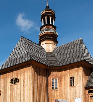 Zdjęcie nr 48: Kościół św. Joachima w Skawinkach usytuowany jest w centrum wsi, na zachód od głównej drogi prowadzącej z Palczy do Kalwarii Zebrzydowskiej. Teren przykościelny jest usytuowany na wysokim wzniesieniu, do którego prowadzą trzy wejścia, jedno przez schody, drugie przez obszerny wjazd od strony południowej.

Kościół skierowany na zachód, drewniany o konstrukcji zrębowej, na rzucie krzyża greckiego ze ściętymi kątami międzyramiennymi.  Przy prezbiterium zakrystia. Strop wsparty na czterech parach słupów, ustawionych w krzyżu kościoła, w licu ścian ramienia wschodniego i zachodniego. Belka tęczy prosta, profilowana na kroksztynach, na niej Grupa Ukrzyżowania. Świątynia połączona za pomocą kruchty z wieżą o konstrukcji słupowej, na planie kwadratu z nadwieszoną izbicą, nakryta dachem namiotowym, ściany dzwonnicy opasane mniej więcej w połowie wysokości pulpitowym daszkiem, zlewającym się po bokach z siodłowym dachem kruchty. Do kościoła prowadzi główne wejście w przedsionku od strony południowej. Wnętrze świątyni oświetlają prostokątne okna. Dach nakryty gontem, na skrzyżowaniu ramiona krzyża greckiego wystawiona wieżyczka na sygnaturkę z latarnią. Ściany na zewnątrz pokryte szalunkiem pionowym.
