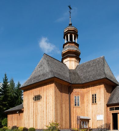 Zdjęcie nr 49: Kościół św. Joachima w Skawinkach usytuowany jest w centrum wsi, na zachód od głównej drogi prowadzącej z Palczy do Kalwarii Zebrzydowskiej. Teren przykościelny jest usytuowany na wysokim wzniesieniu, do którego prowadzą trzy wejścia, jedno przez schody, drugie przez obszerny wjazd od strony południowej.

Kościół skierowany na zachód, drewniany o konstrukcji zrębowej, na rzucie krzyża greckiego ze ściętymi kątami międzyramiennymi.  Przy prezbiterium zakrystia. Strop wsparty na czterech parach słupów, ustawionych w krzyżu kościoła, w licu ścian ramienia wschodniego i zachodniego. Belka tęczy prosta, profilowana na kroksztynach, na niej Grupa Ukrzyżowania. Świątynia połączona za pomocą kruchty z wieżą o konstrukcji słupowej, na planie kwadratu z nadwieszoną izbicą, nakryta dachem namiotowym, ściany dzwonnicy opasane mniej więcej w połowie wysokości pulpitowym daszkiem, zlewającym się po bokach z siodłowym dachem kruchty. Do kościoła prowadzi główne wejście w przedsionku od strony południowej. Wnętrze świątyni oświetlają prostokątne okna. Dach nakryty gontem, na skrzyżowaniu ramiona krzyża greckiego wystawiona wieżyczka na sygnaturkę z latarnią. Ściany na zewnątrz pokryte szalunkiem pionowym.
