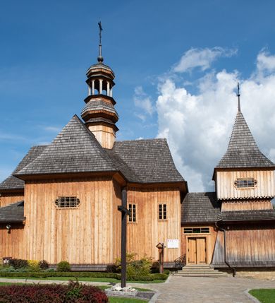 Zdjęcie nr 50: Kościół św. Joachima w Skawinkach usytuowany jest w centrum wsi, na zachód od głównej drogi prowadzącej z Palczy do Kalwarii Zebrzydowskiej. Teren przykościelny jest usytuowany na wysokim wzniesieniu, do którego prowadzą trzy wejścia, jedno przez schody, drugie przez obszerny wjazd od strony południowej.

Kościół skierowany na zachód, drewniany o konstrukcji zrębowej, na rzucie krzyża greckiego ze ściętymi kątami międzyramiennymi.  Przy prezbiterium zakrystia. Strop wsparty na czterech parach słupów, ustawionych w krzyżu kościoła, w licu ścian ramienia wschodniego i zachodniego. Belka tęczy prosta, profilowana na kroksztynach, na niej Grupa Ukrzyżowania. Świątynia połączona za pomocą kruchty z wieżą o konstrukcji słupowej, na planie kwadratu z nadwieszoną izbicą, nakryta dachem namiotowym, ściany dzwonnicy opasane mniej więcej w połowie wysokości pulpitowym daszkiem, zlewającym się po bokach z siodłowym dachem kruchty. Do kościoła prowadzi główne wejście w przedsionku od strony południowej. Wnętrze świątyni oświetlają prostokątne okna. Dach nakryty gontem, na skrzyżowaniu ramiona krzyża greckiego wystawiona wieżyczka na sygnaturkę z latarnią. Ściany na zewnątrz pokryte szalunkiem pionowym.
