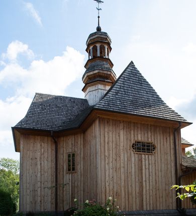 Zdjęcie nr 54: Kościół św. Joachima w Skawinkach usytuowany jest w centrum wsi, na zachód od głównej drogi prowadzącej z Palczy do Kalwarii Zebrzydowskiej. Teren przykościelny jest usytuowany na wysokim wzniesieniu, do którego prowadzą trzy wejścia, jedno przez schody, drugie przez obszerny wjazd od strony południowej.

Kościół skierowany na zachód, drewniany o konstrukcji zrębowej, na rzucie krzyża greckiego ze ściętymi kątami międzyramiennymi.  Przy prezbiterium zakrystia. Strop wsparty na czterech parach słupów, ustawionych w krzyżu kościoła, w licu ścian ramienia wschodniego i zachodniego. Belka tęczy prosta, profilowana na kroksztynach, na niej Grupa Ukrzyżowania. Świątynia połączona za pomocą kruchty z wieżą o konstrukcji słupowej, na planie kwadratu z nadwieszoną izbicą, nakryta dachem namiotowym, ściany dzwonnicy opasane mniej więcej w połowie wysokości pulpitowym daszkiem, zlewającym się po bokach z siodłowym dachem kruchty. Do kościoła prowadzi główne wejście w przedsionku od strony południowej. Wnętrze świątyni oświetlają prostokątne okna. Dach nakryty gontem, na skrzyżowaniu ramiona krzyża greckiego wystawiona wieżyczka na sygnaturkę z latarnią. Ściany na zewnątrz pokryte szalunkiem pionowym.
