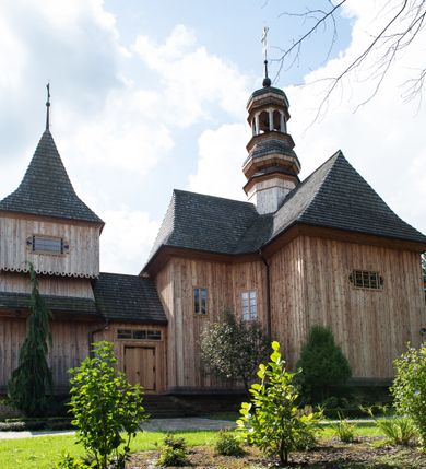 Zdjęcie nr 53: Kościół św. Joachima w Skawinkach usytuowany jest w centrum wsi, na zachód od głównej drogi prowadzącej z Palczy do Kalwarii Zebrzydowskiej. Teren przykościelny jest usytuowany na wysokim wzniesieniu, do którego prowadzą trzy wejścia, jedno przez schody, drugie przez obszerny wjazd od strony południowej.

Kościół skierowany na zachód, drewniany o konstrukcji zrębowej, na rzucie krzyża greckiego ze ściętymi kątami międzyramiennymi.  Przy prezbiterium zakrystia. Strop wsparty na czterech parach słupów, ustawionych w krzyżu kościoła, w licu ścian ramienia wschodniego i zachodniego. Belka tęczy prosta, profilowana na kroksztynach, na niej Grupa Ukrzyżowania. Świątynia połączona za pomocą kruchty z wieżą o konstrukcji słupowej, na planie kwadratu z nadwieszoną izbicą, nakryta dachem namiotowym, ściany dzwonnicy opasane mniej więcej w połowie wysokości pulpitowym daszkiem, zlewającym się po bokach z siodłowym dachem kruchty. Do kościoła prowadzi główne wejście w przedsionku od strony południowej. Wnętrze świątyni oświetlają prostokątne okna. Dach nakryty gontem, na skrzyżowaniu ramiona krzyża greckiego wystawiona wieżyczka na sygnaturkę z latarnią. Ściany na zewnątrz pokryte szalunkiem pionowym.
