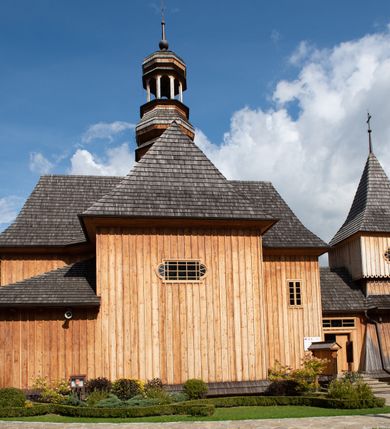 Zdjęcie nr 57: Kościół św. Joachima w Skawinkach usytuowany jest w centrum wsi, na zachód od głównej drogi prowadzącej z Palczy do Kalwarii Zebrzydowskiej. Teren przykościelny jest usytuowany na wysokim wzniesieniu, do którego prowadzą trzy wejścia, jedno przez schody, drugie przez obszerny wjazd od strony południowej.

Kościół skierowany na zachód, drewniany o konstrukcji zrębowej, na rzucie krzyża greckiego ze ściętymi kątami międzyramiennymi.  Przy prezbiterium zakrystia. Strop wsparty na czterech parach słupów, ustawionych w krzyżu kościoła, w licu ścian ramienia wschodniego i zachodniego. Belka tęczy prosta, profilowana na kroksztynach, na niej Grupa Ukrzyżowania. Świątynia połączona za pomocą kruchty z wieżą o konstrukcji słupowej, na planie kwadratu z nadwieszoną izbicą, nakryta dachem namiotowym, ściany dzwonnicy opasane mniej więcej w połowie wysokości pulpitowym daszkiem, zlewającym się po bokach z siodłowym dachem kruchty. Do kościoła prowadzi główne wejście w przedsionku od strony południowej. Wnętrze świątyni oświetlają prostokątne okna. Dach nakryty gontem, na skrzyżowaniu ramiona krzyża greckiego wystawiona wieżyczka na sygnaturkę z latarnią. Ściany na zewnątrz pokryte szalunkiem pionowym.
