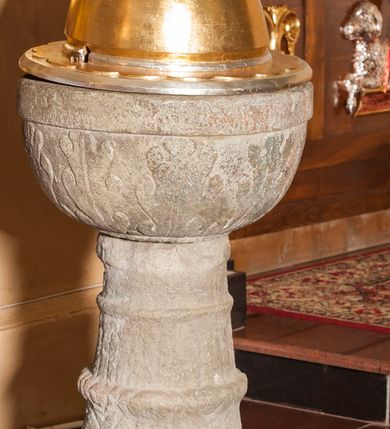 Zdjęcie nr 2: Chrzcielnica kamienna o formie kielichowej, składająca się z czary z pokrywą, trzonu oraz stopy. Stopa okrągłą, stanowiąca pierwotnie część żaren, w formie walca z otworem przy brzegu. Na niej zwężający się trzon złożony z nodusa i pierścieni. Na nodusie ornament plecionkowy, na pierścieniu lancetowate liście. Czara półokrągła, pokryta dekoracją z liści akantu, z gładką krawędzią i wydrążonym zagłębieniem na misę. Pokrywa drewniana, wysoka, półkolista, z szerokim otokiem dekorowanym półkolami; zwęża się ku górze. Rozbudowane zwieńczenie dekorowane od dołu kolejno koronką zakończoną półkoliście, puklowaniem, motywem płomieni oraz profilowanym trzonem zakończonym dużą szyszką. Chrzcielnica w kolorze kamienia, gdzieniegdzie pozostałości czerwonej farby, pokrywa złocona i srebrzona. 