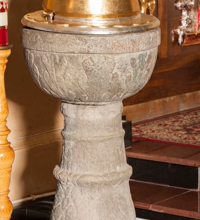 Zdjęcie nr 1: Chrzcielnica kamienna o formie kielichowej, składająca się z czary z pokrywą, trzonu oraz stopy. Stopa okrągłą, stanowiąca pierwotnie część żaren, w formie walca z otworem przy brzegu. Na niej zwężający się trzon złożony z nodusa i pierścieni. Na nodusie ornament plecionkowy, na pierścieniu lancetowate liście. Czara półokrągła, pokryta dekoracją z liści akantu, z gładką krawędzią i wydrążonym zagłębieniem na misę. Pokrywa drewniana, wysoka, półkolista, z szerokim otokiem dekorowanym półkolami; zwęża się ku górze. Rozbudowane zwieńczenie dekorowane od dołu kolejno koronką zakończoną półkoliście, puklowaniem, motywem płomieni oraz profilowanym trzonem zakończonym dużą szyszką. Chrzcielnica w kolorze kamienia, gdzieniegdzie pozostałości czerwonej farby, pokrywa złocona i srebrzona. 