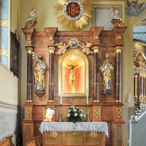 Zdjęcie nr 1: Nastawa ołtarzowa architektoniczna, trójosiowa, jednokondygnacyjna ze zwieńczeniem, na cokole. Mensa skrzyniowa, z antepedium artykułowanym trzema prostokątnymi płycinami, w bocznych rozety, w środkowej krzyż równoramienny. Cokół nastawy siedmiodzielny, z nieparzystymi częściami wysuniętymi przed lico, zdobionymi plakietami ornamentalnymi. Nastawa dzielona kolumnami z opaskami w jednej trzeciej wysokości, o kapitelach utworzonych z elementów roślinnych, podtrzymujących belkowanie wyłamane na ich osiach. W wyłamanych częściach fryzu plakiety dekoracyjne z motywem roślinnym. W polu centralnym nisza z rzeźbą ukrzyżowanego Chrystusa między narzędziami męki, oprawiona w szeroką, profilowaną ramę. Powyżej niej para putt trzymająca kartusz obwiedziony ramą z kwitnących róż z napisem „JEZU / ZMIŁUJ SIĘ / NAD / NAMI”. W polach bocznych ustawione na konsolach i cokołach figury św. Józefa po lewej i św. Joachima (?) po prawej stronie. W partii zwieńczenia urwane fragmenty przyczółka ponad zewnętrznymi fragmentami belkowania, na nich posadowione modlące się postacie. Na środku, w okrągłym polu monogram IHS otoczony obłokami, na tle glorii promienistej. 
Ołtarz marmoryzowany na kolor jasnobrązowy, płyciny na kolor brązowo-żółty, kolumny na ciemnobrązowy. Detale i ornamenty złocone; polichromia w partiach ciała postaci naturalistyczna. 