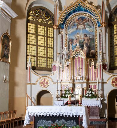 Zdjęcie nr 2: Ołtarz przyścienny z obejściem, złożony z mensy, predelli, bramek i nastawy. Mensa sarkofagowa, z kamiennym blatem, antepedium haftowane w motywy roślinne, z barankiem paschalnym w centrum. Predella dwukondygnacyjna, trójosiowa, osie rozdzielają zdwojone kolumny na wysokich konsolach, wychodzące przed lico predelli. W dolnej partii, części boczne dekorowane płycinami o kształcie zbliżonym do kwadratu, złożone z czworoliści, w polu środkowym prostopadłościenne tabernakulum, z drzwiczkami dekorowanymi groszowaniem i umieszczonym na jego tle motywem zdwojonego łuku ostrego z wpisanym monogramem IHS. Górna kondygnacja predelli oddzielona gzymsem, złożona z trzech zakończonych ostrołukowo blend w centrum i pięciu płycin różnej wysokości w częściach bocznych, flankowana pinaklami. Oś środkowa zakończona łukiem w ośli grzbiet nałożonym na łuk okrągły, zdobionym żabkami i zwieńczona krzyżem, flankowanym pinaklami z żabkami i kwiatonem. Do predelli przylegają z dwóch stron bramki prostokątne, zamknięte od góry łukiem odwróconym i flankowane pinaklem zakończonym kwiatonem. W bramkach wycięty otwór w kształcie prostokąta zamkniętego łukiem pełnym, powyżej którego umieszczono okrągłą plakietę wypełnioną motywem czworoliścia z wpisanymi łukami podkowiastymi. Plakietę ujmuje od góry łuk nadwieszony stykający się w środkowej części ze wspomnianym łukiem odwróconym. Nastawa znajduje się za predellą. Widoczna część składa się z pola flankowanego smukłymi kolumnami o kapitelach utworzonych z motywów roślinnych, na których skośnie ustawiono pinakle zdobione żabkami i zwieńczone kwiatonami. Na kolumnach wspiera się łuk w ośli grzbiet zdobiony od dołu ażurową koronką, a od góry żabkami i zwieńczony krzyżem. Za kolumnami ustawiono niższe, smuklejsze i skręcone, nakryte baldachimami z wyciętymi łukami ostrymi. Pole nastawy wypełnia obraz z przedstawieniem chrztu Chrystusa w kształcie stojącego prostokąta zamkniętego półkoliście w ramie utworzonej z mięsistych liści. 
Powierzchnia ołtarza w kolorze białym, wnętrza płycin czerwone, profile, detale i ornamenty złocone, wnętrze arkady nastawy niebieskie. 