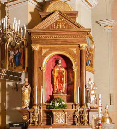 Zdjęcie nr 1: Ołtarz przyścienny, architektoniczny, jednoosiowy, jednokondygnacyjny. Mensa skrzyniowa z kamiennym portatylem, poprzedzona dwoma, masywnymi kolumienkami o kostkowych kapitelach. Antepedium artykułowane czterema prostokątnymi płycinami zamkniętymi półkoliście. Na mensie, na kolumienkach blat ołtarza. Na nim prostopadłościenne tabernakulum, z drzwiczkami akcentowanymi płyciną w kształcie prostokąta zamkniętego półkoliście. Na drzwiach aplikowane, złączone ze sobą symbole: kielich z hostią, gorejące serce, krzyż i kotwica na tle obłoków. Cokół nastawy ołtarza pięciodzielny, z płycinami. Wysunięte osie cokołu są dekorowane plakietą z motywem roślinnym, zaś skrajne są ozdobione konsolami z aplikowaną, okrągłą rozetą. Pole środkowe z prostokątną wnęką zamkniętą półkoliście, z łukiem wspartym na dwóch kolumnach korynckich. We wnęce na czerwonym tle figura Najświętszego Serca Pana Jezusa. W narożach plakiety ornamentalne w trójkątnych polach. Nastawa flankowana parą kolumn korynckich ustawionych na wysuniętych partiach cokołu oraz figurami świętych. Kolumny wspierają belkowanie zwieńczone trójkątnym przyczółkiem wypełnionym chrystogramem. Za tympanonem pozłacana kopuła pokryta motywem rybiej łuski, zwieńczona krzyżem postawionym na rozecie. Całość ołtarza fladrowana w odcieniu ciemnobrązowym, ornamenty i detal architektoniczny złocony, polichromia rzeźb naturalistyczna.