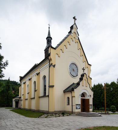 Zdjęcie nr 2: Kościół orientowany, jednonawowy, czteroprzęsłowy z niższym i węższym, jednoprzęsłowym prezbiterium zamkniętym wielobocznie. Od północnego wschodu do prezbiterium i nawy przylega zakrystia na rzucie prostokąta, od południowego wschodu prostokątna kruchta, a od zachodu kolejna prostokątna kruchta. W nawie sklepienie kolebkowe z lunetami, na zdwojonych gurtach przechodzących w pilastry o kompozytowych kapitelach i kanelowanych trzonach; w prezbiterium kolebkowe z lunetami na pojedynczych gurtach. Prezbiterium od nawy wydziela ściana tęczowa otwierająca się do wnętrza półkolistą arkadą. W ostatnim, zachodnim przęśle nawy chór muzyczny o ażurowej balustradzie, wsparty na dwóch smukłych, żeliwnych kolumnach. Otwory okienne w nawie i prezbiterium w kształcie stojącego prostokąta zamkniętego półkoliście. W ścianie zachodniej, w osi elewacji okno okrągłe. Fasada jednokondygnacyjna, jednoosiowa zamknięta trójkątną ścianą szczytową zwieńczoną krzyżem osadzonym na niewielkim daszku. W przyziemiu kruchta z otworem wejściowym w kształcie stojącego prostokąta zamkniętego łukiem półkolistym. Drzwi drewniane, dwuskrzydłowe z nadświetlem. Elewacja kruchty zamknięta schodkową ścianą szczytową zwieńczoną kamiennym krzyżem. Powyżej duże, okrągłe okno wypełnione rozetą, ujęte w motyw półkolistej arkady zaznaczonej w tynku. W górnej części fasady fryz arkadkowy. Elewacje boczne artykułowane uskokowymi przyporami, w górnej części dekorowane fryzem arkadowym. Nad nawą dach dwuspadowy, nad prezbiterium wielopołaciowy, ponad zakrystią oraz obiema kruchtami jednospadowy. Wszystkie kryte blachą. Ponad nawą umieszczona czworoboczna wieżyczka na sygnaturkę, z glorietą zwieńczoną ostrosłupowym hełmem. Na jej szczycie ażurowy krzyż. Elewacje świątyni tynkowane w odcieniach koloru żółtego oraz bieli.