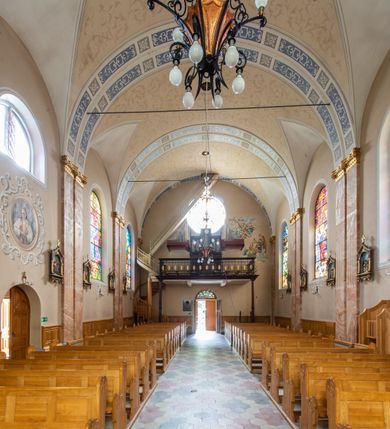 Zdjęcie nr 9: Kościół orientowany, jednonawowy, czteroprzęsłowy z niższym i węższym, jednoprzęsłowym prezbiterium zamkniętym wielobocznie. Od północnego wschodu do prezbiterium i nawy przylega zakrystia na rzucie prostokąta, od południowego wschodu prostokątna kruchta, a od zachodu kolejna prostokątna kruchta. W nawie sklepienie kolebkowe z lunetami, na zdwojonych gurtach przechodzących w pilastry o kompozytowych kapitelach i kanelowanych trzonach; w prezbiterium kolebkowe z lunetami na pojedynczych gurtach. Prezbiterium od nawy wydziela ściana tęczowa otwierająca się do wnętrza półkolistą arkadą. W ostatnim, zachodnim przęśle nawy chór muzyczny o ażurowej balustradzie, wsparty na dwóch smukłych, żeliwnych kolumnach. Otwory okienne w nawie i prezbiterium w kształcie stojącego prostokąta zamkniętego półkoliście. W ścianie zachodniej, w osi elewacji okno okrągłe. Fasada jednokondygnacyjna, jednoosiowa zamknięta trójkątną ścianą szczytową zwieńczoną krzyżem osadzonym na niewielkim daszku. W przyziemiu kruchta z otworem wejściowym w kształcie stojącego prostokąta zamkniętego łukiem półkolistym. Drzwi drewniane, dwuskrzydłowe z nadświetlem. Elewacja kruchty zamknięta schodkową ścianą szczytową zwieńczoną kamiennym krzyżem. Powyżej duże, okrągłe okno wypełnione rozetą, ujęte w motyw półkolistej arkady zaznaczonej w tynku. W górnej części fasady fryz arkadkowy. Elewacje boczne artykułowane uskokowymi przyporami, w górnej części dekorowane fryzem arkadowym. Nad nawą dach dwuspadowy, nad prezbiterium wielopołaciowy, ponad zakrystią oraz obiema kruchtami jednospadowy. Wszystkie kryte blachą. Ponad nawą umieszczona czworoboczna wieżyczka na sygnaturkę, z glorietą zwieńczoną ostrosłupowym hełmem. Na jej szczycie ażurowy krzyż. Elewacje świątyni tynkowane w odcieniach koloru żółtego oraz bieli.