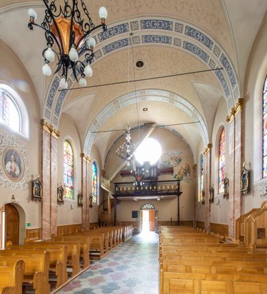 Zdjęcie nr 10: Kościół orientowany, jednonawowy, czteroprzęsłowy z niższym i węższym, jednoprzęsłowym prezbiterium zamkniętym wielobocznie. Od północnego wschodu do prezbiterium i nawy przylega zakrystia na rzucie prostokąta, od południowego wschodu prostokątna kruchta, a od zachodu kolejna prostokątna kruchta. W nawie sklepienie kolebkowe z lunetami, na zdwojonych gurtach przechodzących w pilastry o kompozytowych kapitelach i kanelowanych trzonach; w prezbiterium kolebkowe z lunetami na pojedynczych gurtach. Prezbiterium od nawy wydziela ściana tęczowa otwierająca się do wnętrza półkolistą arkadą. W ostatnim, zachodnim przęśle nawy chór muzyczny o ażurowej balustradzie, wsparty na dwóch smukłych, żeliwnych kolumnach. Otwory okienne w nawie i prezbiterium w kształcie stojącego prostokąta zamkniętego półkoliście. W ścianie zachodniej, w osi elewacji okno okrągłe. Fasada jednokondygnacyjna, jednoosiowa zamknięta trójkątną ścianą szczytową zwieńczoną krzyżem osadzonym na niewielkim daszku. W przyziemiu kruchta z otworem wejściowym w kształcie stojącego prostokąta zamkniętego łukiem półkolistym. Drzwi drewniane, dwuskrzydłowe z nadświetlem. Elewacja kruchty zamknięta schodkową ścianą szczytową zwieńczoną kamiennym krzyżem. Powyżej duże, okrągłe okno wypełnione rozetą, ujęte w motyw półkolistej arkady zaznaczonej w tynku. W górnej części fasady fryz arkadkowy. Elewacje boczne artykułowane uskokowymi przyporami, w górnej części dekorowane fryzem arkadowym. Nad nawą dach dwuspadowy, nad prezbiterium wielopołaciowy, ponad zakrystią oraz obiema kruchtami jednospadowy. Wszystkie kryte blachą. Ponad nawą umieszczona czworoboczna wieżyczka na sygnaturkę, z glorietą zwieńczoną ostrosłupowym hełmem. Na jej szczycie ażurowy krzyż. Elewacje świątyni tynkowane w odcieniach koloru żółtego oraz bieli.