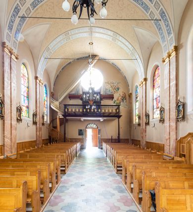 Zdjęcie nr 12: Kościół orientowany, jednonawowy, czteroprzęsłowy z niższym i węższym, jednoprzęsłowym prezbiterium zamkniętym wielobocznie. Od północnego wschodu do prezbiterium i nawy przylega zakrystia na rzucie prostokąta, od południowego wschodu prostokątna kruchta, a od zachodu kolejna prostokątna kruchta. W nawie sklepienie kolebkowe z lunetami, na zdwojonych gurtach przechodzących w pilastry o kompozytowych kapitelach i kanelowanych trzonach; w prezbiterium kolebkowe z lunetami na pojedynczych gurtach. Prezbiterium od nawy wydziela ściana tęczowa otwierająca się do wnętrza półkolistą arkadą. W ostatnim, zachodnim przęśle nawy chór muzyczny o ażurowej balustradzie, wsparty na dwóch smukłych, żeliwnych kolumnach. Otwory okienne w nawie i prezbiterium w kształcie stojącego prostokąta zamkniętego półkoliście. W ścianie zachodniej, w osi elewacji okno okrągłe. Fasada jednokondygnacyjna, jednoosiowa zamknięta trójkątną ścianą szczytową zwieńczoną krzyżem osadzonym na niewielkim daszku. W przyziemiu kruchta z otworem wejściowym w kształcie stojącego prostokąta zamkniętego łukiem półkolistym. Drzwi drewniane, dwuskrzydłowe z nadświetlem. Elewacja kruchty zamknięta schodkową ścianą szczytową zwieńczoną kamiennym krzyżem. Powyżej duże, okrągłe okno wypełnione rozetą, ujęte w motyw półkolistej arkady zaznaczonej w tynku. W górnej części fasady fryz arkadkowy. Elewacje boczne artykułowane uskokowymi przyporami, w górnej części dekorowane fryzem arkadowym. Nad nawą dach dwuspadowy, nad prezbiterium wielopołaciowy, ponad zakrystią oraz obiema kruchtami jednospadowy. Wszystkie kryte blachą. Ponad nawą umieszczona czworoboczna wieżyczka na sygnaturkę, z glorietą zwieńczoną ostrosłupowym hełmem. Na jej szczycie ażurowy krzyż. Elewacje świątyni tynkowane w odcieniach koloru żółtego oraz bieli.