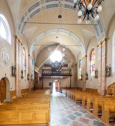 Zdjęcie nr 13: Kościół orientowany, jednonawowy, czteroprzęsłowy z niższym i węższym, jednoprzęsłowym prezbiterium zamkniętym wielobocznie. Od północnego wschodu do prezbiterium i nawy przylega zakrystia na rzucie prostokąta, od południowego wschodu prostokątna kruchta, a od zachodu kolejna prostokątna kruchta. W nawie sklepienie kolebkowe z lunetami, na zdwojonych gurtach przechodzących w pilastry o kompozytowych kapitelach i kanelowanych trzonach; w prezbiterium kolebkowe z lunetami na pojedynczych gurtach. Prezbiterium od nawy wydziela ściana tęczowa otwierająca się do wnętrza półkolistą arkadą. W ostatnim, zachodnim przęśle nawy chór muzyczny o ażurowej balustradzie, wsparty na dwóch smukłych, żeliwnych kolumnach. Otwory okienne w nawie i prezbiterium w kształcie stojącego prostokąta zamkniętego półkoliście. W ścianie zachodniej, w osi elewacji okno okrągłe. Fasada jednokondygnacyjna, jednoosiowa zamknięta trójkątną ścianą szczytową zwieńczoną krzyżem osadzonym na niewielkim daszku. W przyziemiu kruchta z otworem wejściowym w kształcie stojącego prostokąta zamkniętego łukiem półkolistym. Drzwi drewniane, dwuskrzydłowe z nadświetlem. Elewacja kruchty zamknięta schodkową ścianą szczytową zwieńczoną kamiennym krzyżem. Powyżej duże, okrągłe okno wypełnione rozetą, ujęte w motyw półkolistej arkady zaznaczonej w tynku. W górnej części fasady fryz arkadkowy. Elewacje boczne artykułowane uskokowymi przyporami, w górnej części dekorowane fryzem arkadowym. Nad nawą dach dwuspadowy, nad prezbiterium wielopołaciowy, ponad zakrystią oraz obiema kruchtami jednospadowy. Wszystkie kryte blachą. Ponad nawą umieszczona czworoboczna wieżyczka na sygnaturkę, z glorietą zwieńczoną ostrosłupowym hełmem. Na jej szczycie ażurowy krzyż. Elewacje świątyni tynkowane w odcieniach koloru żółtego oraz bieli.