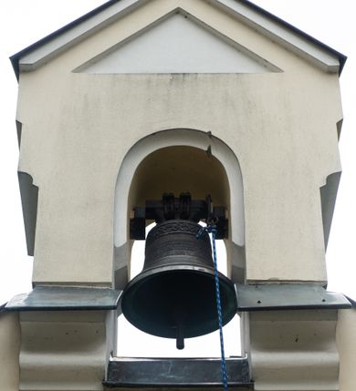 Zdjęcie nr 2: Murowana i tynkowana, wolnostojąca dzwonnica o formach architektonicznych, dwuosiowa i dwukondygnacyjna. Kondygnacja pierwsza umieszczona na niewysokim cokole, dwuosiowa, zamknięta po bokach dwuspadowym, profilowanym daszkiem krytym blachą. Elewacja z dwoma półkolistymi arkadami artykułowana wysuniętą przed jej lico lizeną zwieńczoną jednospadowym daszkiem, krytym blachą. Lica arkad zdobione dekoracją w tynku naśladującą ciosy kamienne. W prześwitach arkad zawieszone dwa dzwony. Kondygnacja druga jednoosiowa, zamknięta trójkątnym przyczółkiem z dwuspadowym daszkiem krytym blachą. W prześwicie półkolistej arkady zawieszony dzwon. W zwieńczeniu kamienny krzyż równoramienny o wklęsłej linii ramion.