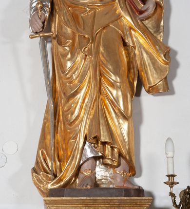 Zdjęcie nr 2: Całopostaciowa, ustawiona na konsoli w formie spływu wolutowego figura przedstawia zwróconą na wprost postać św. Pawła stojącego w lekkim kontrapoście. Pociągłą twarz charakteryzuje długi, ciemnobrązowy zarost, niewielkie, szeroko otwarte oczy wzniesione brwi oraz długi, prosty nos. Włosy są krótkie, ciemnobrązowe, kręcone. Święty ubrany jest w srebrzoną suknię z długimi rękawami oraz osłaniający niemal całą sylwetkę, wydatnie fałdowany złocony płaszcz, na stopach są złocone sandały. Prawą, opuszczoną w dół ręką podtrzymuje wsparty na pole płaszcza miecz, w lewej ma księgę w czerwonej oprawie. 