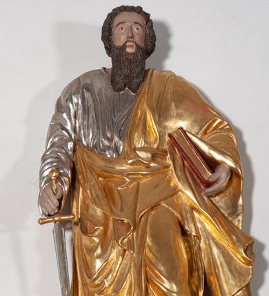 Zdjęcie nr 3: Całopostaciowa, ustawiona na konsoli w formie spływu wolutowego figura przedstawia zwróconą na wprost postać św. Pawła stojącego w lekkim kontrapoście. Pociągłą twarz charakteryzuje długi, ciemnobrązowy zarost, niewielkie, szeroko otwarte oczy wzniesione brwi oraz długi, prosty nos. Włosy są krótkie, ciemnobrązowe, kręcone. Święty ubrany jest w srebrzoną suknię z długimi rękawami oraz osłaniający niemal całą sylwetkę, wydatnie fałdowany złocony płaszcz, na stopach są złocone sandały. Prawą, opuszczoną w dół ręką podtrzymuje wsparty na pole płaszcza miecz, w lewej ma księgę w czerwonej oprawie. 