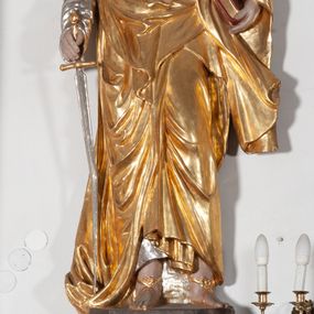 Zdjęcie nr 1: Całopostaciowa, ustawiona na konsoli w formie spływu wolutowego figura przedstawia zwróconą na wprost postać św. Pawła stojącego w lekkim kontrapoście. Pociągłą twarz charakteryzuje długi, ciemnobrązowy zarost, niewielkie, szeroko otwarte oczy wzniesione brwi oraz długi, prosty nos. Włosy są krótkie, ciemnobrązowe, kręcone. Święty ubrany jest w srebrzoną suknię z długimi rękawami oraz osłaniający niemal całą sylwetkę, wydatnie fałdowany złocony płaszcz, na stopach są złocone sandały. Prawą, opuszczoną w dół ręką podtrzymuje wsparty na pole płaszcza miecz, w lewej ma księgę w czerwonej oprawie. 