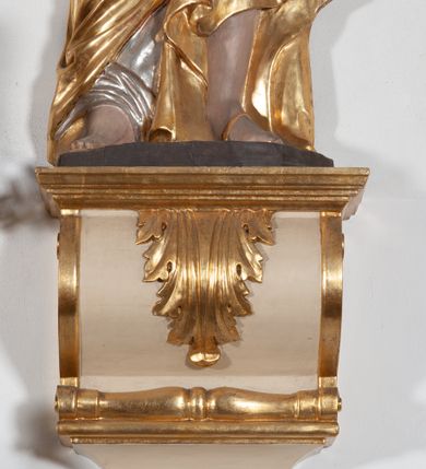 Zdjęcie nr 3: Całopostaciowa, ustawiona na konsoli w formie spływu wolutowego figura przedstawia zwróconą na wprost postać św. Piotra stojącego w lekkim kontrapoście. Owalną twarz charakteryzuje krótki, ciemnobrązowy zarost, niewielkie, szeroko otwarte oczy wzniesione brwi oraz długi, prosty nos. Włosy są krótkie, ciemnobrązowe, kręcone. Święty ubrany jest w srebrzoną suknię z długimi rękawami oraz osłaniający niemal całą sylwetkę, wydatnie fałdowany złocony płaszcz. Prawą, zgiętą w łokciu rękę wznosi do góry w geście błogosławieństwa. Lewą podtrzymuje księgę w czerwonej oprawie, w dłoni ma parę skrzyżowanych, złoconych kluczy.  