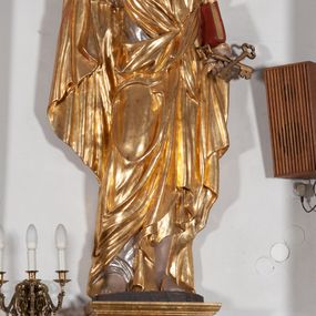 Zdjęcie nr 1: Całopostaciowa, ustawiona na konsoli w formie spływu wolutowego figura przedstawia zwróconą na wprost postać św. Piotra stojącego w lekkim kontrapoście. Owalną twarz charakteryzuje krótki, ciemnobrązowy zarost, niewielkie, szeroko otwarte oczy wzniesione brwi oraz długi, prosty nos. Włosy są krótkie, ciemnobrązowe, kręcone. Święty ubrany jest w srebrzoną suknię z długimi rękawami oraz osłaniający niemal całą sylwetkę, wydatnie fałdowany złocony płaszcz. Prawą, zgiętą w łokciu rękę wznosi do góry w geście błogosławieństwa. Lewą podtrzymuje księgę w czerwonej oprawie, w dłoni ma parę skrzyżowanych, złoconych kluczy.  